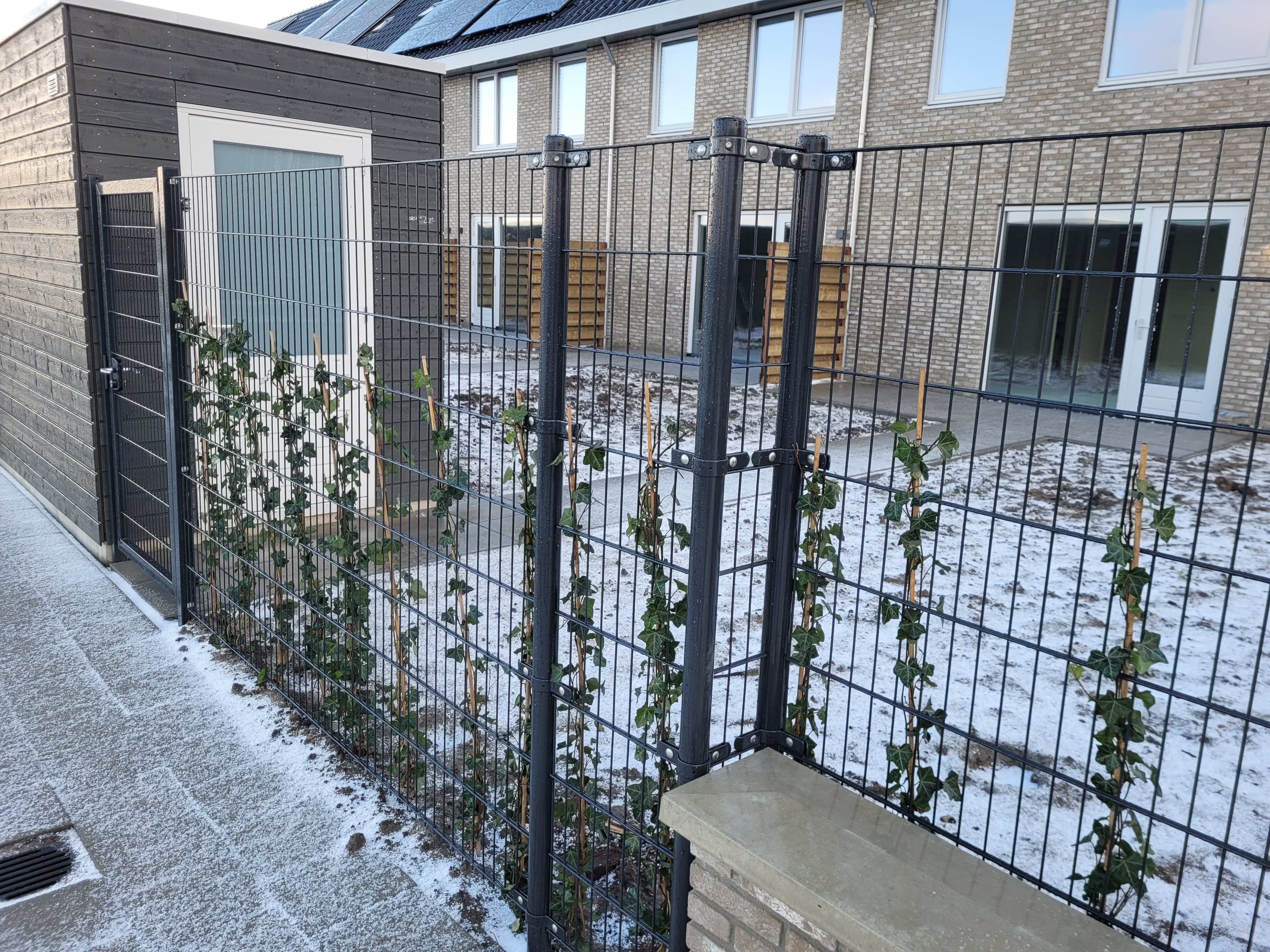 En snødekt hage er omgitt av et vakkert panelgjerde