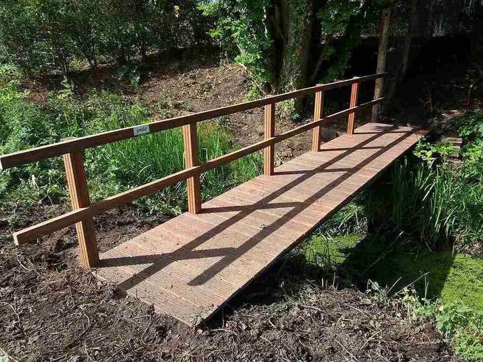 Vakker trebro med rekkverk på den ene siden tar deg trygt over elven