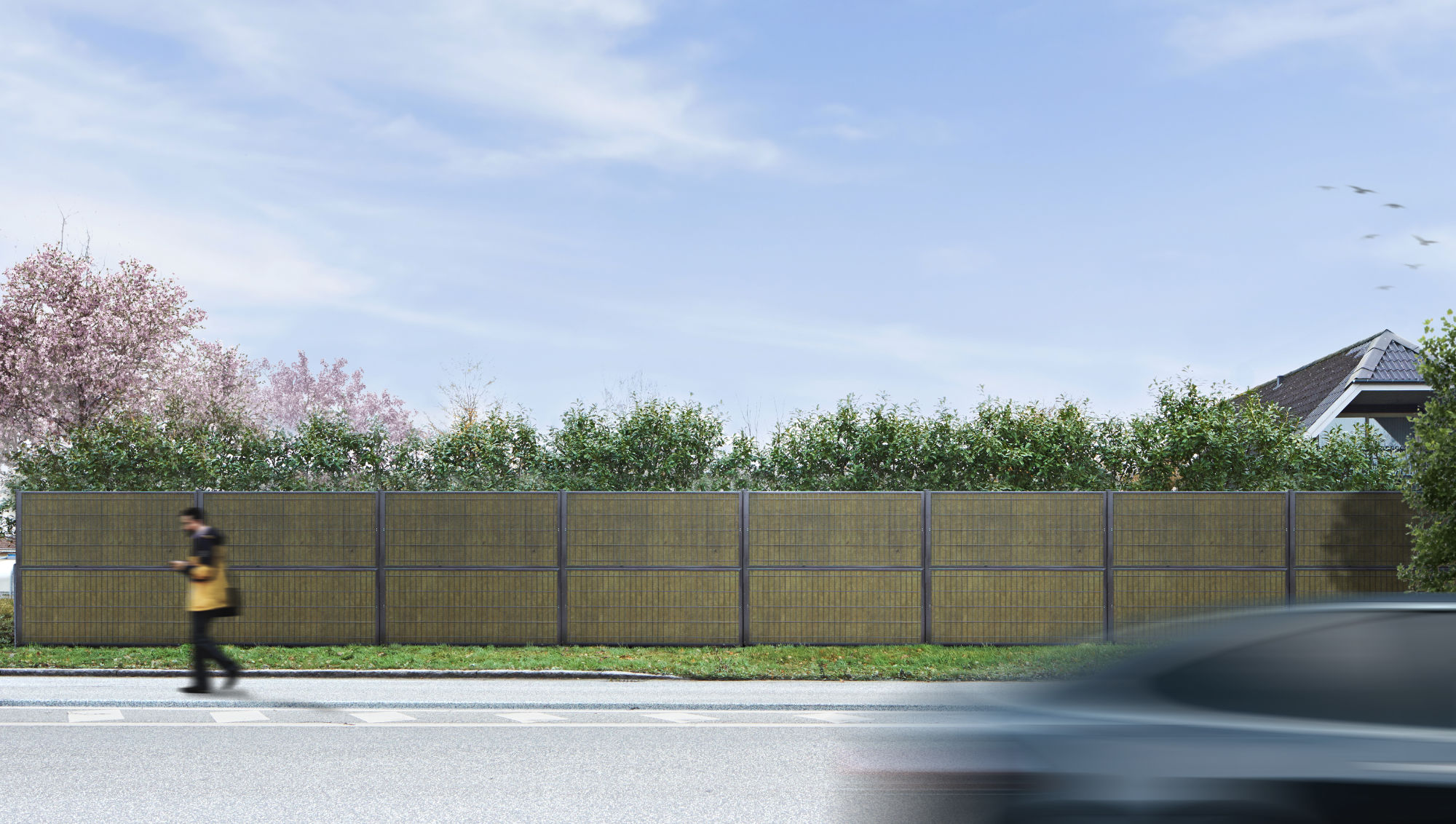 Noistop Essential støygjerde med antrasittgrå ramme, omgitt av grønn beplantning, med en fotgjenger og en forbipasserende bil i forgrunnen.