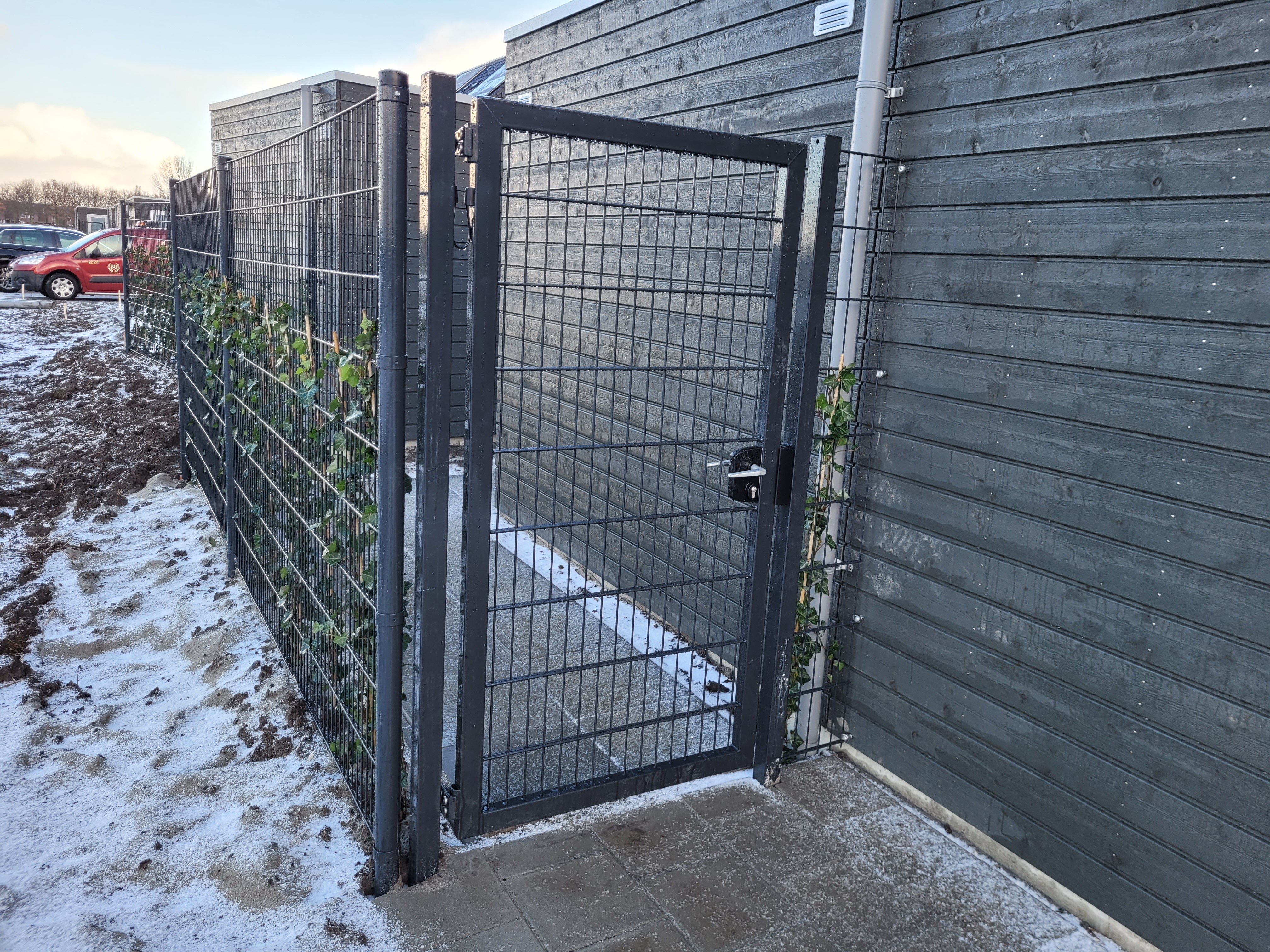 På baksiden av et skur er det installert en grind etterfulgt av et plankegjerde