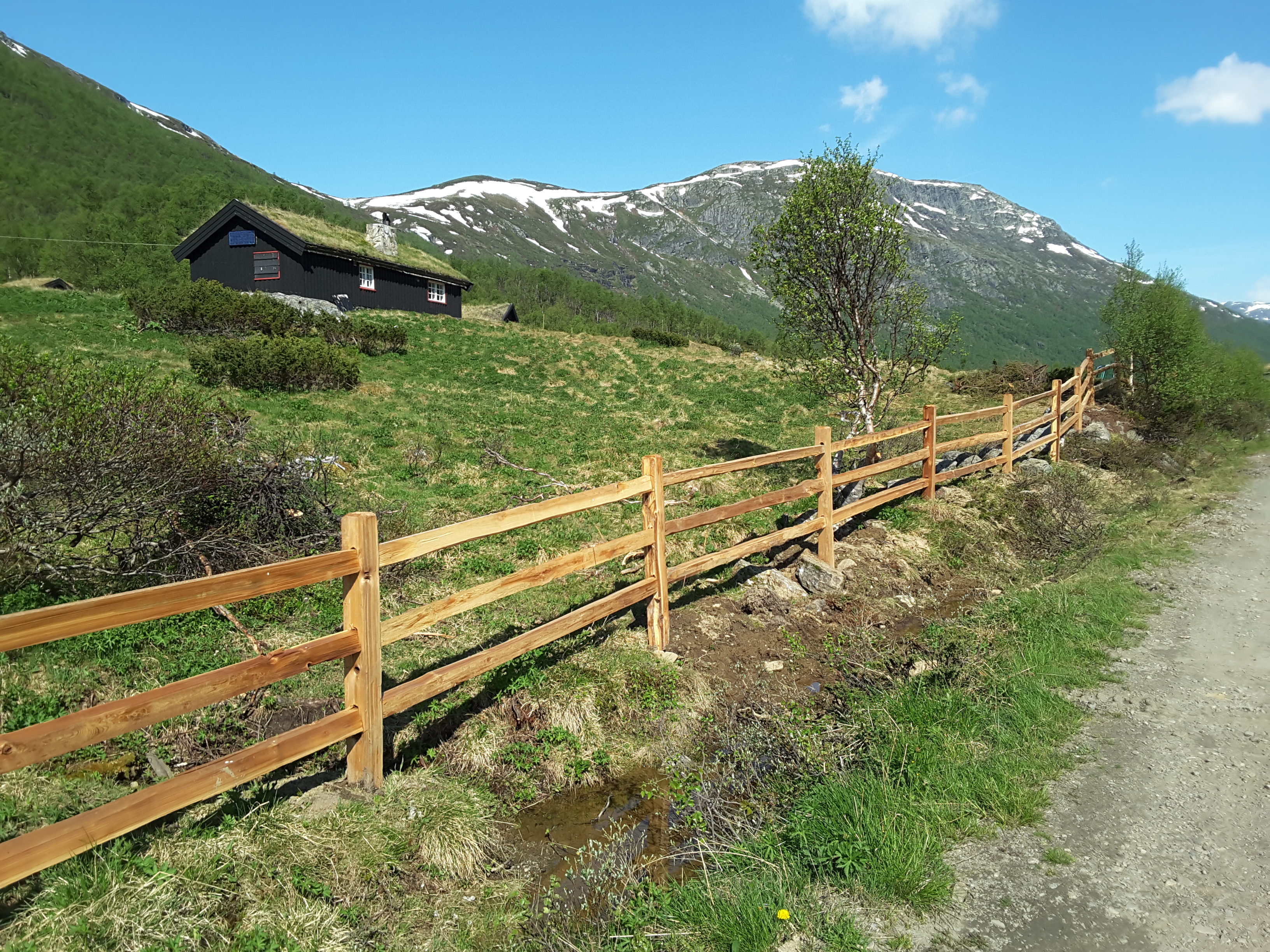 Et rustikt gjerde i sedertre avgrenser en naturtomt med hytte i et fjellområde.