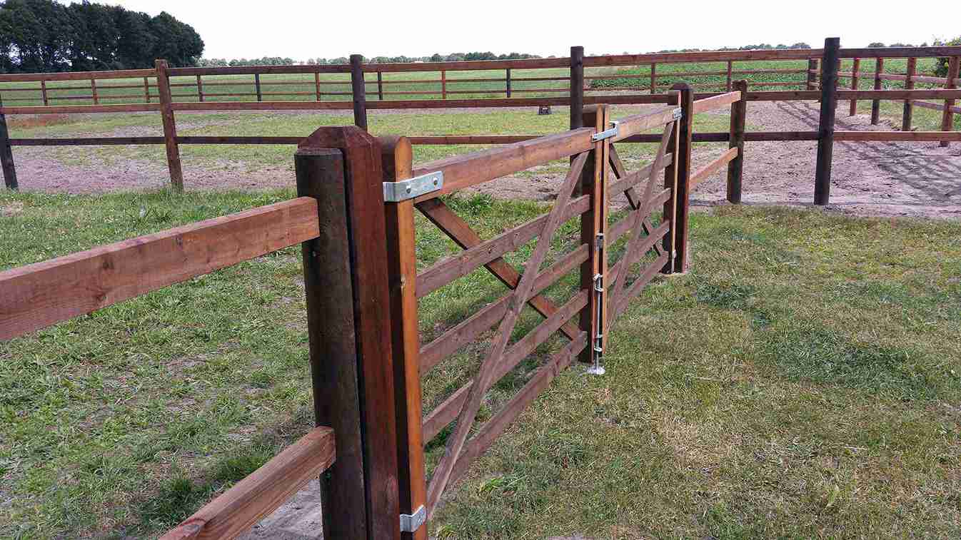 Et hestegjerde skiller to hestepaddocker. En dobbel treport gir tilgang til den ene hesteinnhegningen.