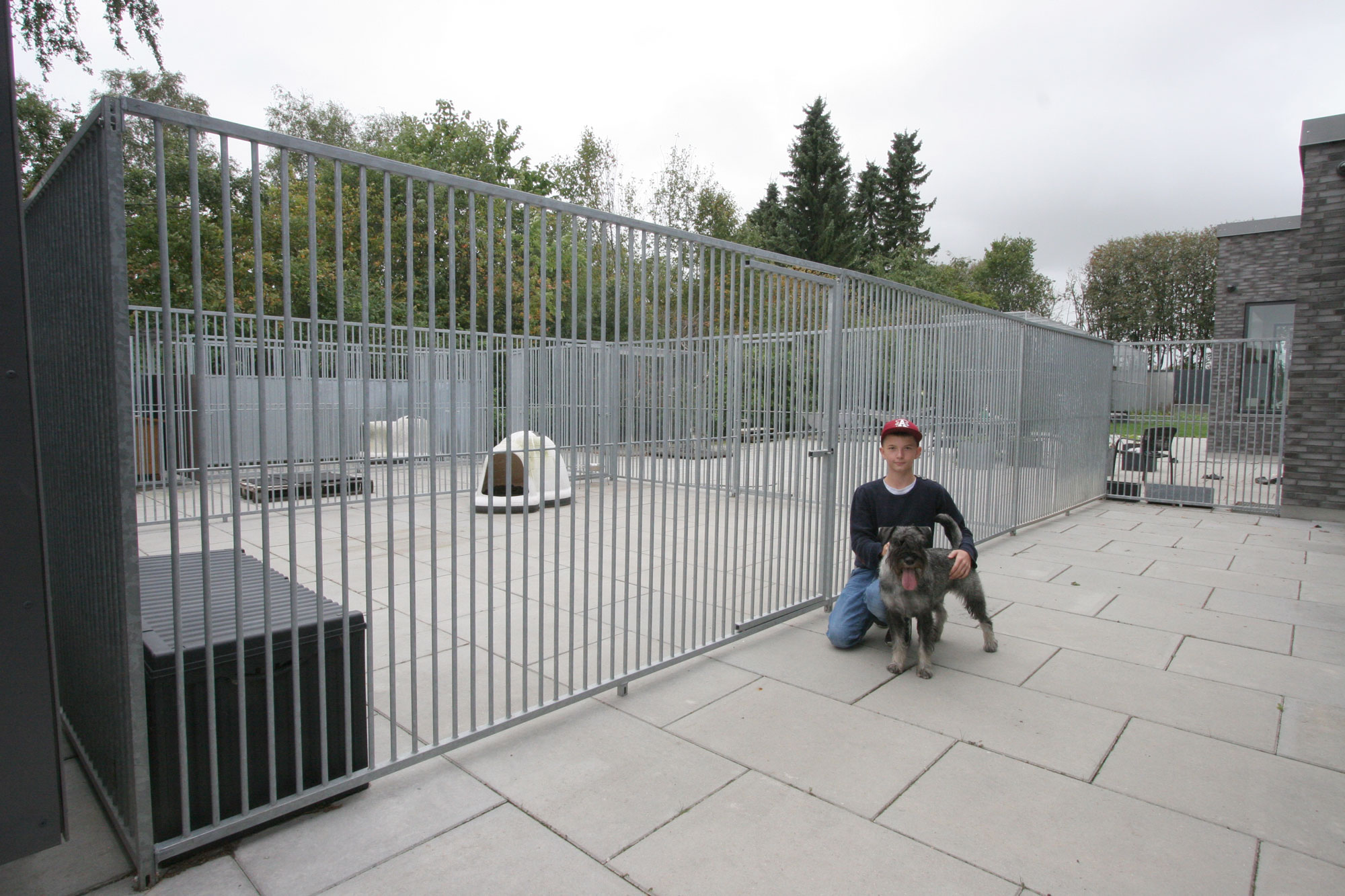 En gutt står på kne foran en hundegård sammen med hunden sin.